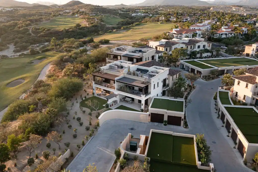 Aerial view of luxury residences along the Palmilla Golf Club fairways with rooftop putting greens, multi-level terraces, and Sierra de la Laguna mountains in the background