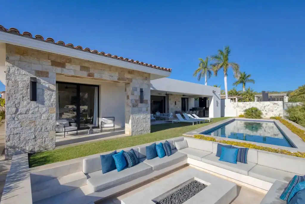 Contemporary hacienda-style residence in Palmilla featuring natural stone facade, sunken fire pit lounge, private pool, and covered outdoor living areas with palm trees